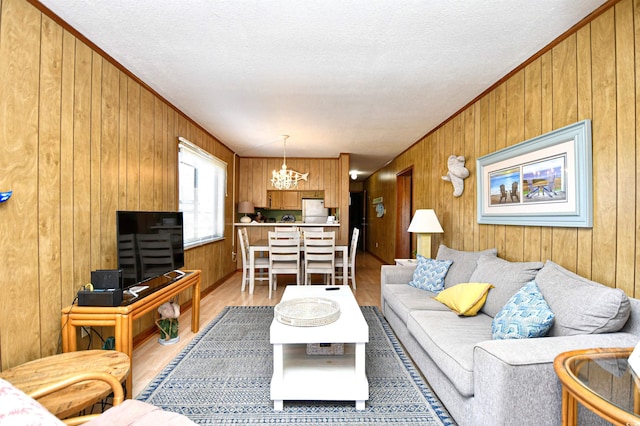 living room with light wood-style floors, a chandelier, crown molding, and wood walls