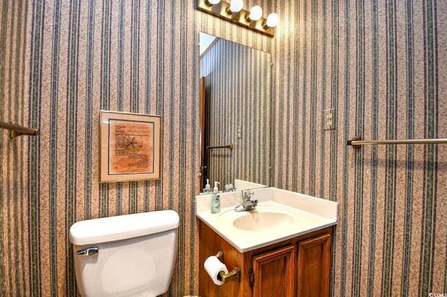 half bathroom featuring vanity, toilet, and wallpapered walls