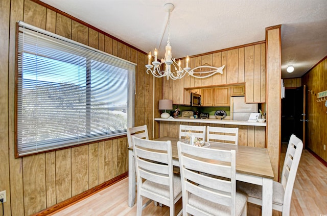 dining area featuring a chandelier, light wood-style flooring, and wooden walls