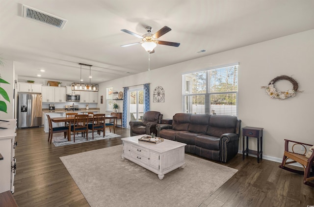 living area featuring a ceiling fan, dark wood-style flooring, visible vents, and baseboards