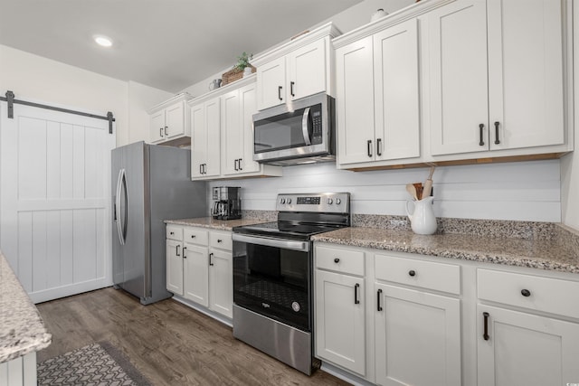 kitchen featuring a barn door, white cabinets, dark wood finished floors, appliances with stainless steel finishes, and light stone counters