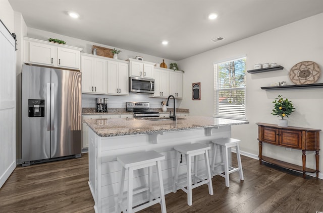 kitchen with dark wood-style floors, a center island with sink, a barn door, appliances with stainless steel finishes, and a sink