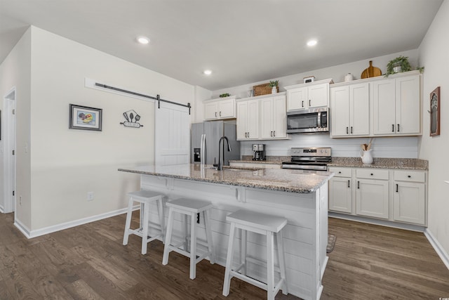 kitchen featuring a barn door, an island with sink, dark wood-style floors, appliances with stainless steel finishes, and a sink