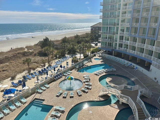 pool with a view of the beach, a community hot tub, a water view, and a patio