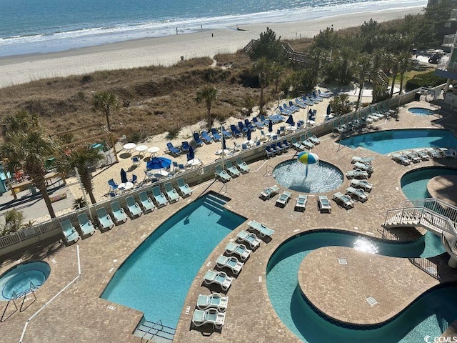 pool with a patio area, a hot tub, and a beach view