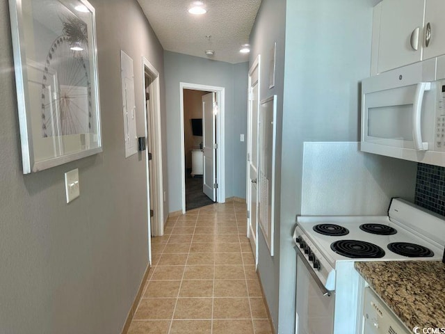 kitchen featuring white appliances, light tile patterned floors, light stone countertops, a textured ceiling, and white cabinetry