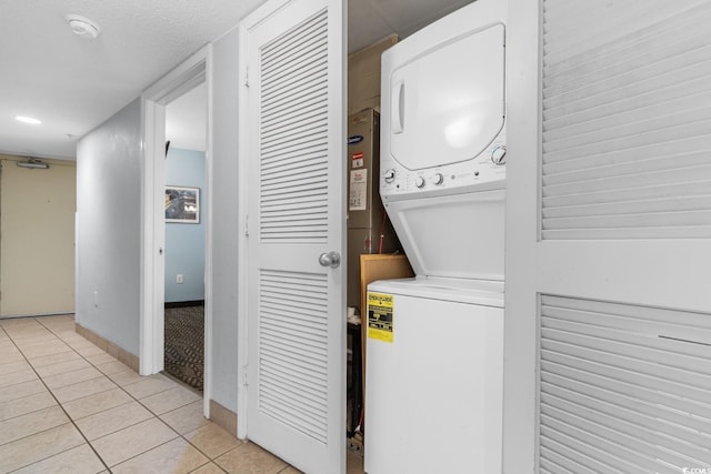 laundry area featuring laundry area, stacked washer / dryer, light tile patterned floors, and baseboards