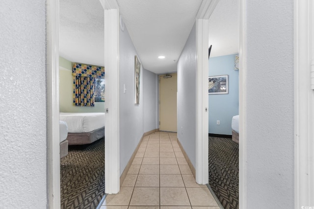 corridor featuring light tile patterned floors, light colored carpet, baseboards, and a textured ceiling