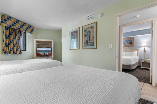 carpeted bedroom with tile patterned flooring, visible vents, and a textured ceiling