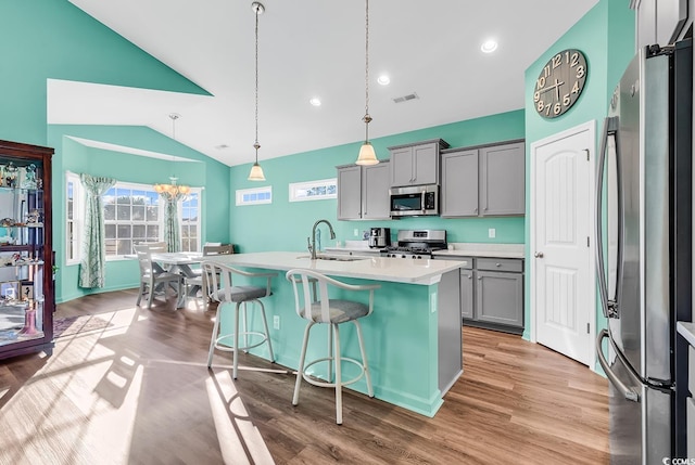 kitchen with gray cabinetry, stainless steel appliances, a sink, vaulted ceiling, and light countertops