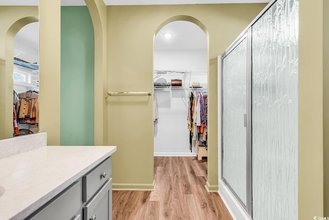 bathroom with a spacious closet, vanity, a shower stall, wood finished floors, and baseboards