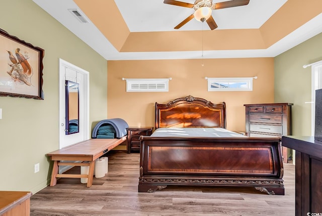 bedroom with a ceiling fan, visible vents, a tray ceiling, and wood finished floors