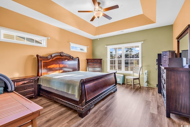 bedroom featuring a tray ceiling, visible vents, ceiling fan, and wood finished floors