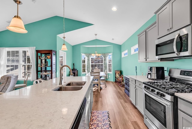 kitchen with lofted ceiling, light stone counters, a sink, light wood-style floors, and appliances with stainless steel finishes