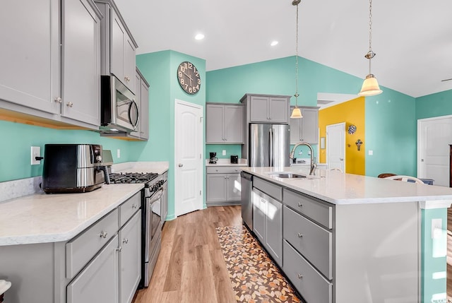 kitchen with a sink, light wood-style floors, hanging light fixtures, appliances with stainless steel finishes, and gray cabinets