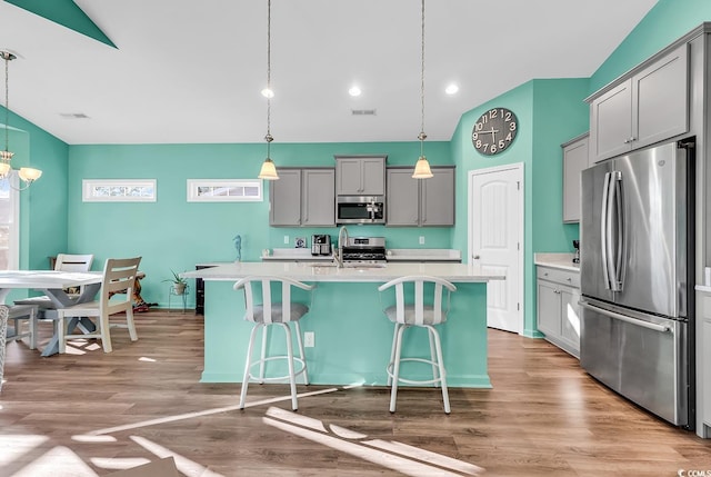 kitchen with appliances with stainless steel finishes, gray cabinets, light countertops, and a kitchen bar