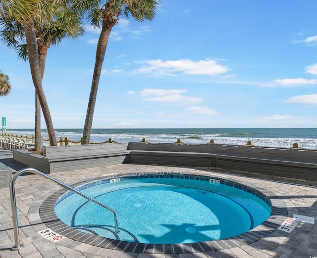 view of swimming pool with a water view, a hot tub, and a view of the beach