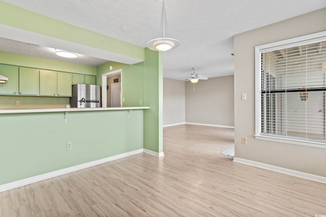 kitchen featuring light wood finished floors, a ceiling fan, freestanding refrigerator, green cabinetry, and baseboards