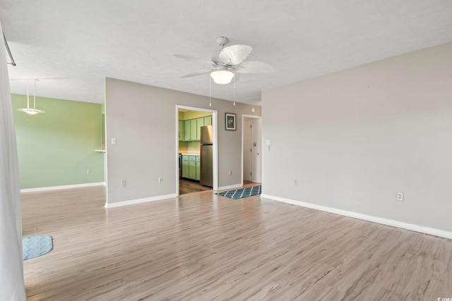 empty room featuring a textured ceiling, wood finished floors, a ceiling fan, and baseboards