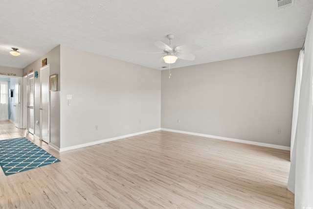 empty room with visible vents, light wood-style floors, a ceiling fan, a textured ceiling, and baseboards