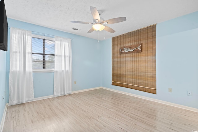 empty room with baseboards, visible vents, a ceiling fan, wood finished floors, and a textured ceiling