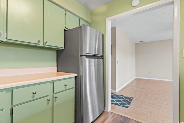 kitchen featuring freestanding refrigerator, baseboards, light wood-style flooring, and green cabinets