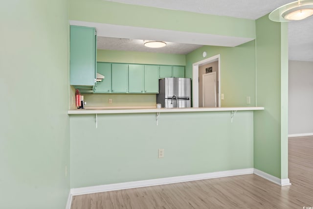 kitchen with a breakfast bar area, green cabinets, freestanding refrigerator, wood finished floors, and baseboards