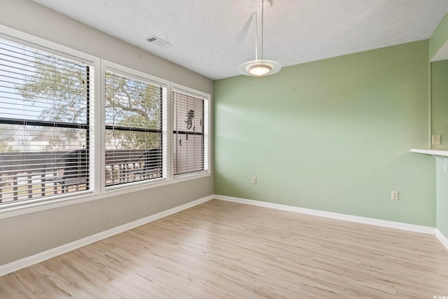 empty room featuring a textured ceiling, light wood-style floors, visible vents, and baseboards