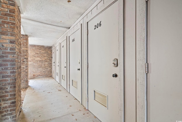 hallway featuring brick wall, visible vents, and a textured ceiling