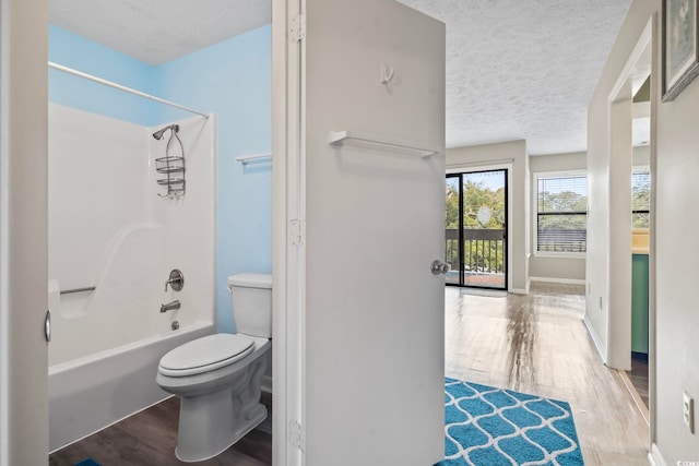 bathroom featuring a textured ceiling, shower / bath combination, wood finished floors, and toilet