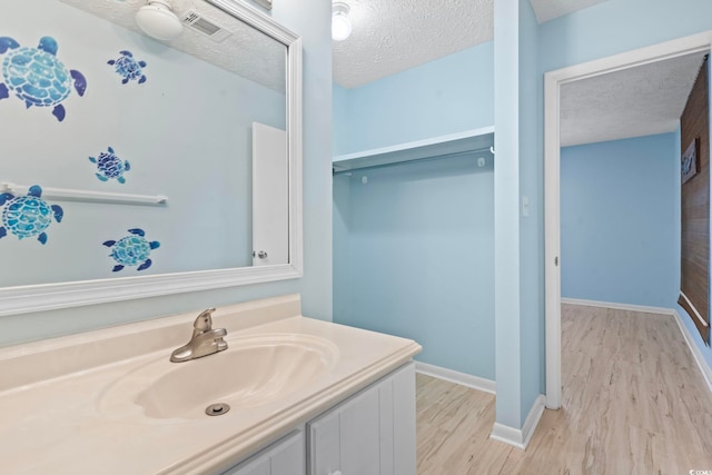 bathroom featuring visible vents, a textured ceiling, vanity, wood finished floors, and baseboards