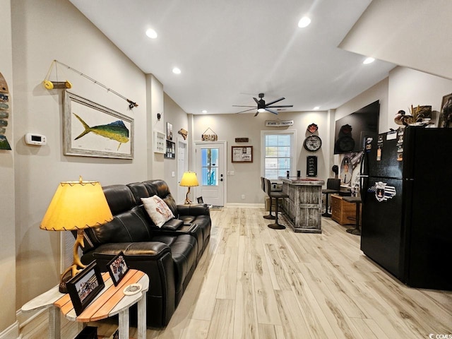 living area featuring baseboards, ceiling fan, a bar, light wood-style floors, and recessed lighting