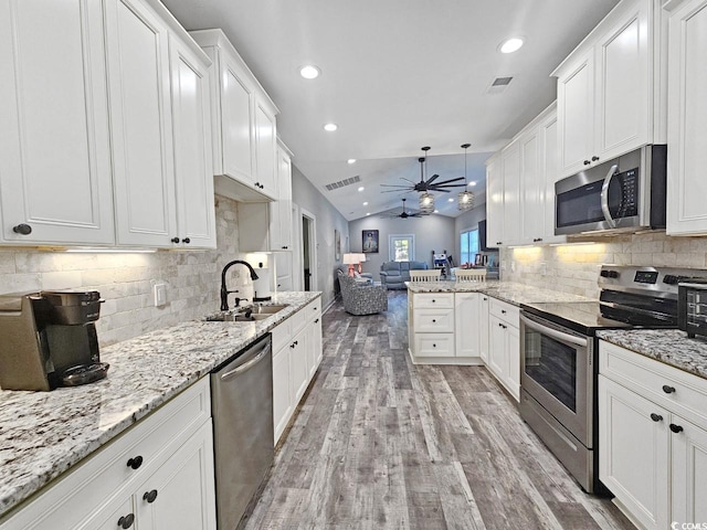 kitchen featuring white cabinets, lofted ceiling, appliances with stainless steel finishes, open floor plan, and a sink