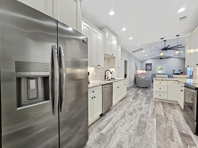 kitchen with light wood finished floors, stainless steel appliances, backsplash, a sink, and vaulted ceiling