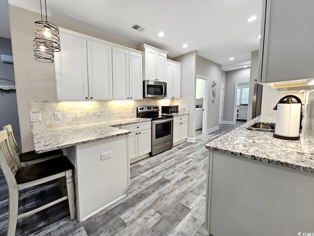 kitchen with a peninsula, white cabinetry, visible vents, appliances with stainless steel finishes, and decorative backsplash