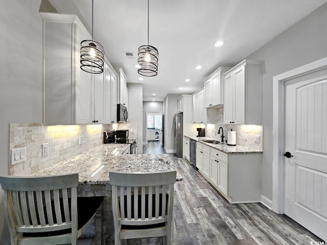 kitchen with tasteful backsplash, appliances with stainless steel finishes, light stone counters, wood finished floors, and white cabinetry