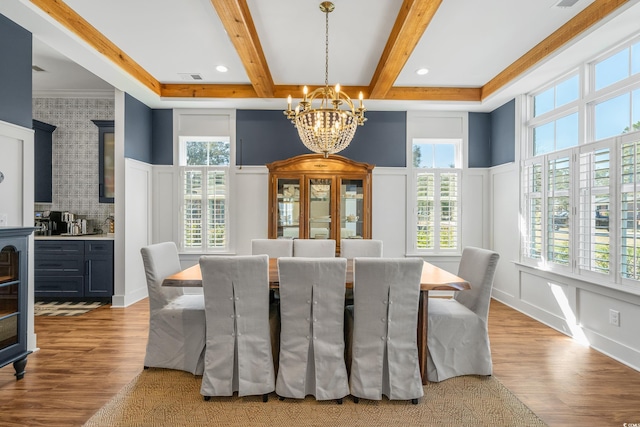 dining room with a chandelier, beamed ceiling, light wood-style flooring, and a decorative wall