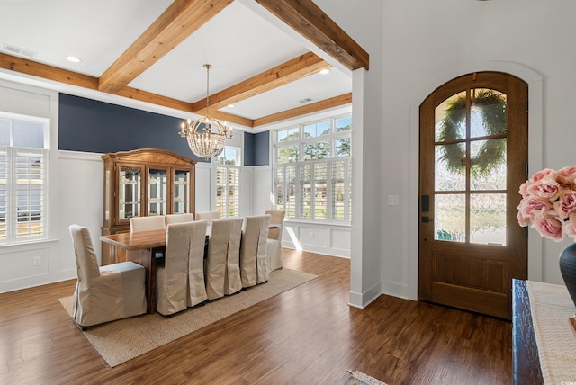 dining space with a notable chandelier, a decorative wall, beamed ceiling, and wood finished floors