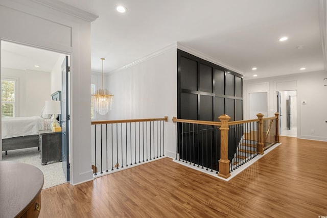 corridor with recessed lighting, wood finished floors, an upstairs landing, ornamental molding, and an inviting chandelier