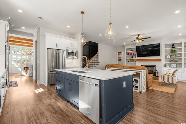 kitchen with a fireplace, crown molding, stainless steel appliances, white cabinetry, and a sink