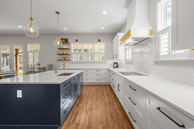 kitchen featuring black electric stovetop, custom range hood, backsplash, white cabinetry, and a sink