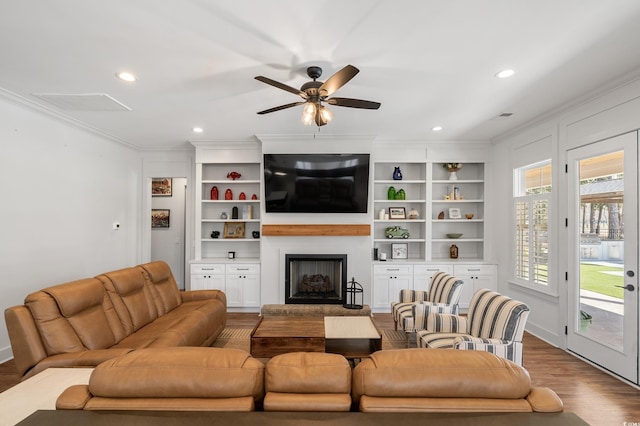 living room with crown molding, recessed lighting, a fireplace with raised hearth, a ceiling fan, and wood finished floors