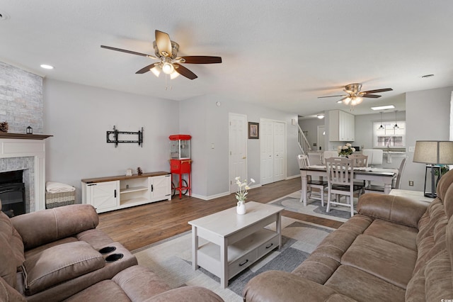 living room with wood finished floors, a large fireplace, baseboards, ceiling fan, and stairs