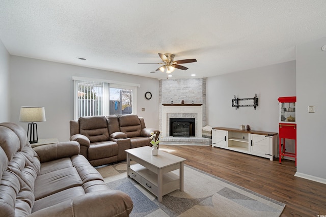 living room featuring a ceiling fan, a textured ceiling, wood finished floors, and a fireplace