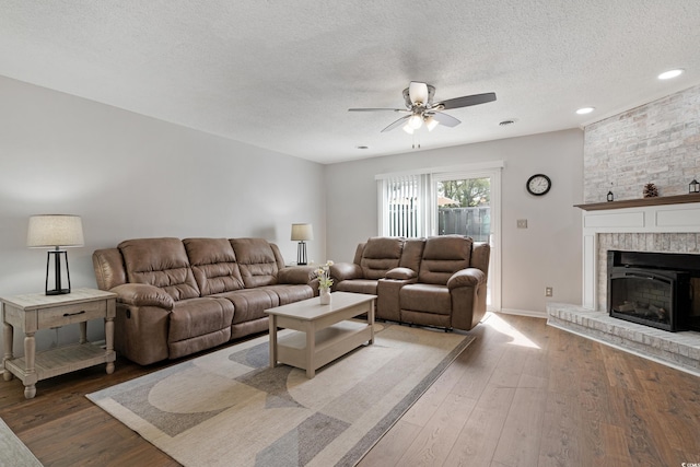 living area featuring a ceiling fan, a textured ceiling, recessed lighting, wood-type flooring, and a fireplace