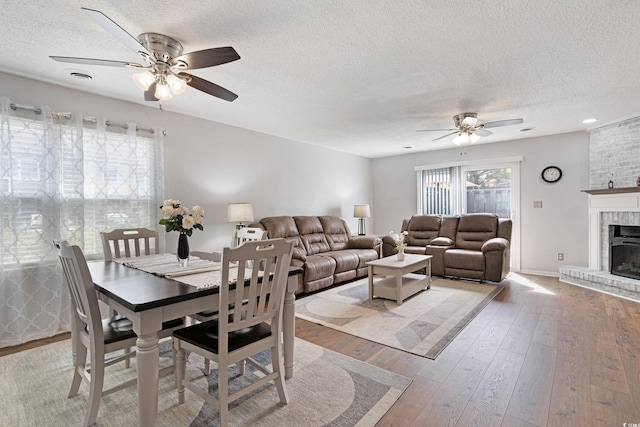 dining space with visible vents, ceiling fan, hardwood / wood-style floors, a fireplace, and a textured ceiling