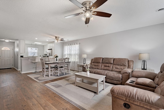 living room featuring visible vents, hardwood / wood-style flooring, a textured ceiling, baseboards, and ceiling fan