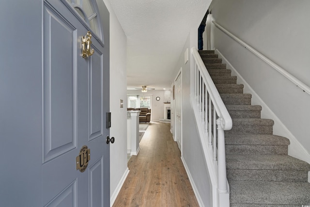 entrance foyer featuring a fireplace with raised hearth, a textured ceiling, wood finished floors, baseboards, and stairs