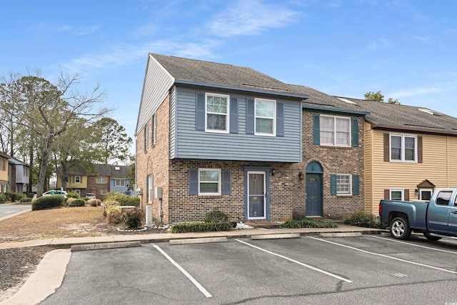 view of property with brick siding, uncovered parking, and roof with shingles