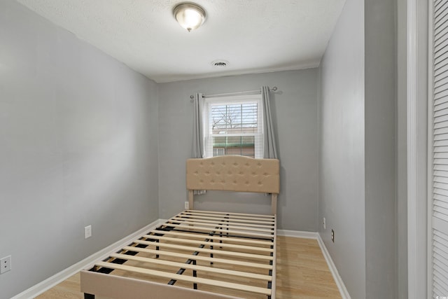 unfurnished bedroom with a textured ceiling, visible vents, baseboards, and light wood-type flooring